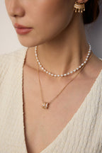 Model wearing layered pearl choker and delicate 14k gold plated pendant necklace with textured gold hoop earring
