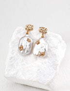 Mira Aura baroque pearl pendant earrings with gold floral accents on textured white stone