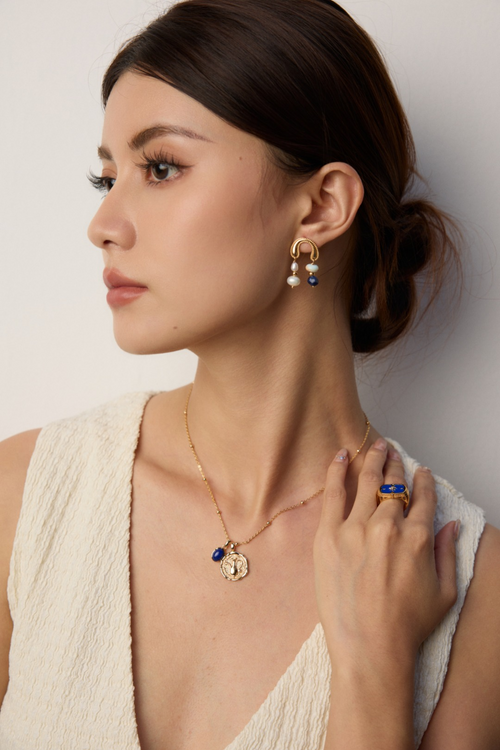 Model wearing gold plated gemstone necklace with blue stone pendant and matching gold earrings and ring
