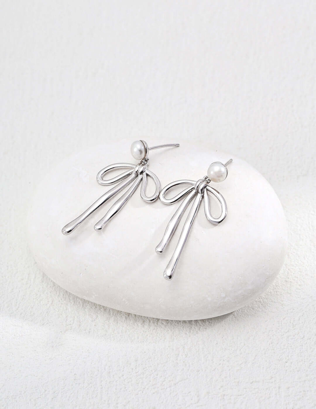 modern gold dangle earrings shown in silver tone with pearl studs and flowing looped strands on white stone