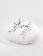 modern gold dangle earrings shown in silver tone with pearl studs and flowing looped strands on white stone
