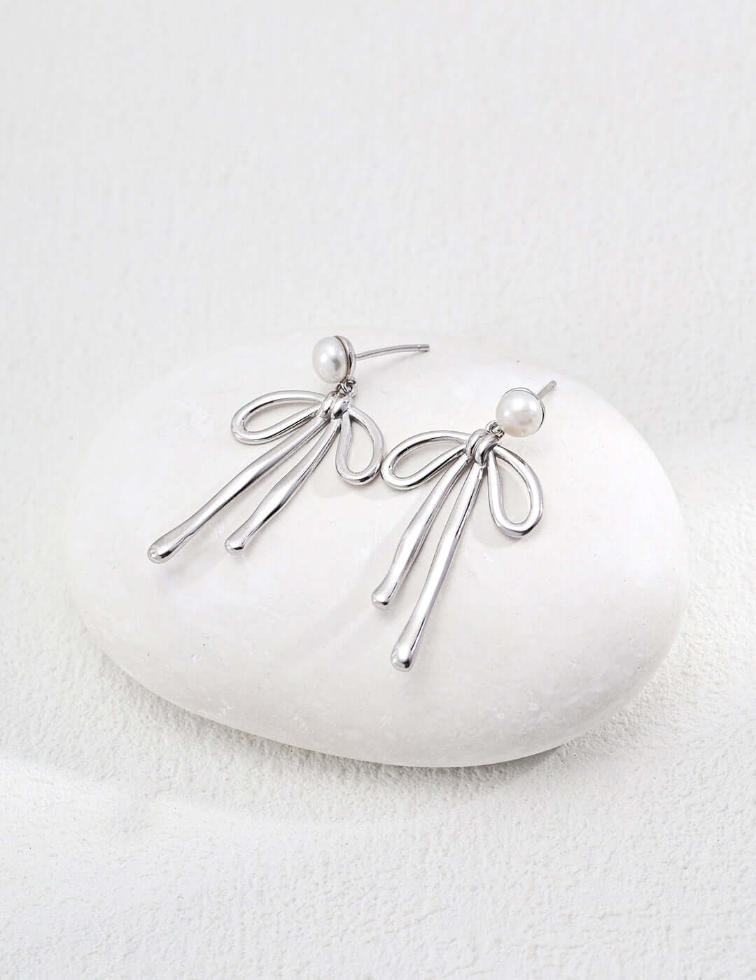 modern gold dangle earrings shown in silver tone with pearl studs and flowing looped strands on white stone