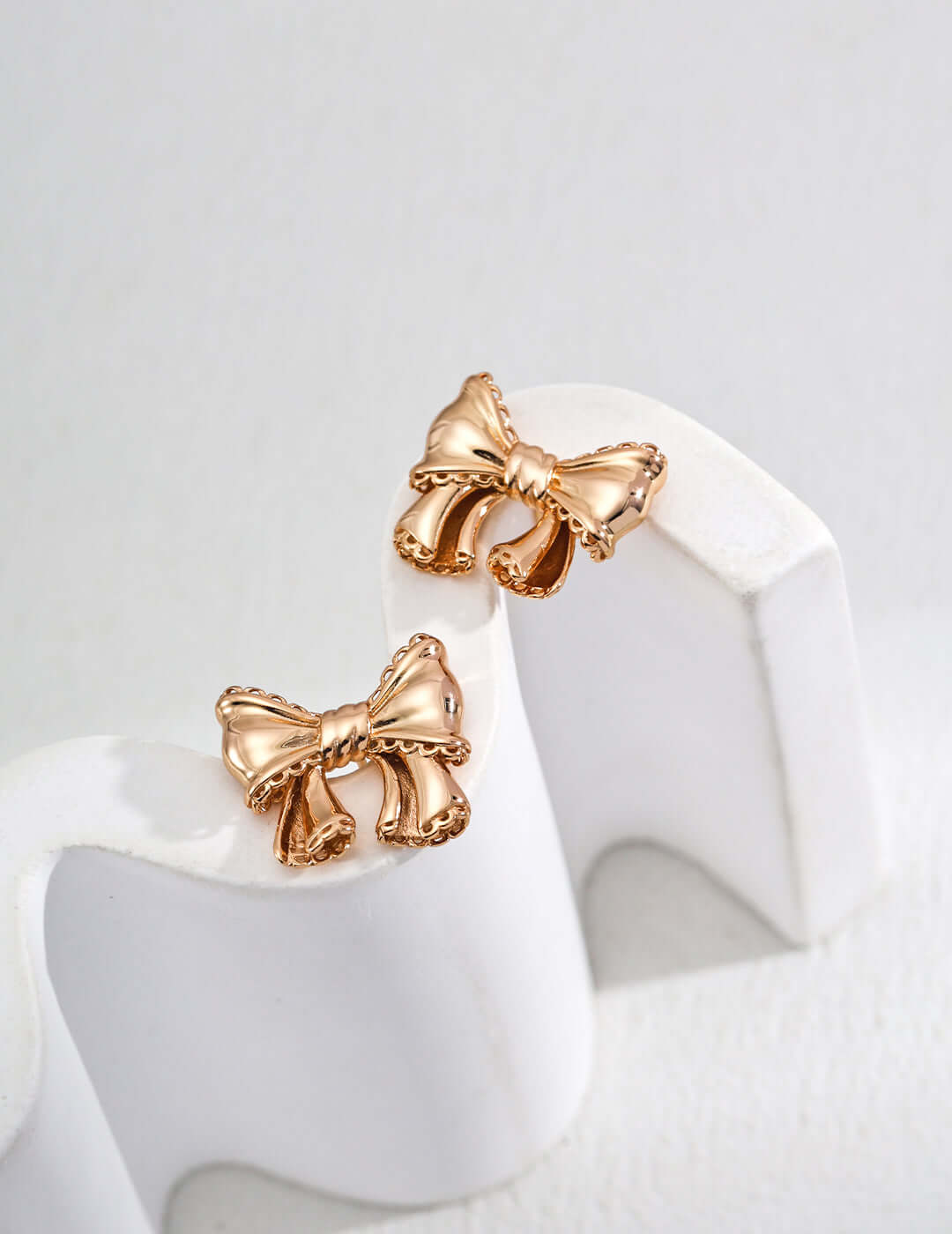 Mira Aura modern gold knot earrings bow shaped polished gold stud earrings on white display stand