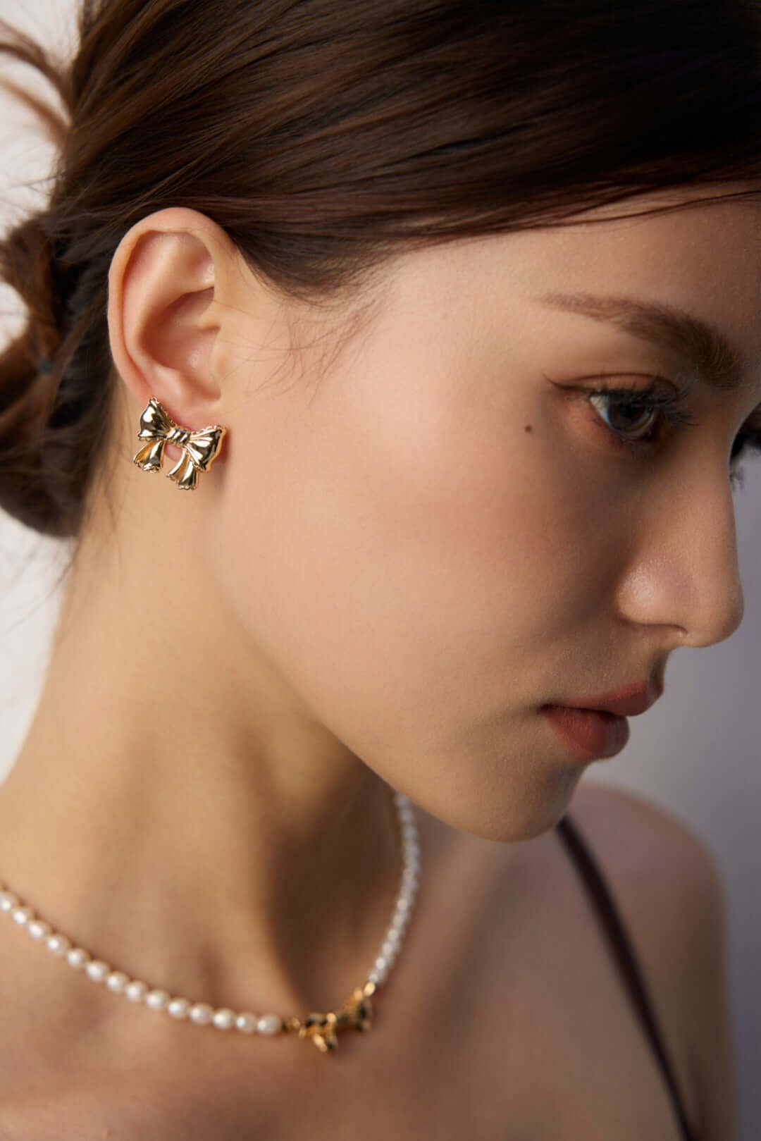 Close up side profile of model wearing modern gold knot earrings with pearl necklace for elegant styling