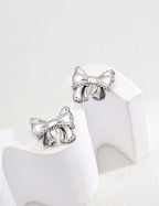 Mira Aura modern gold knot earrings product photo showing silver bow knot stud earrings on white stand