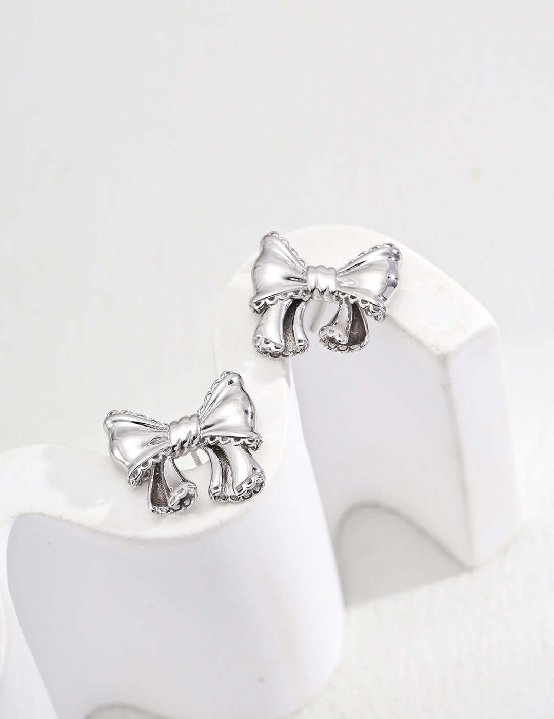 Mira Aura modern gold knot earrings product photo showing silver bow knot stud earrings on white stand