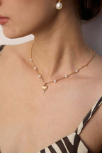 Model wearing gold plated heart pendant necklace with pearl station chain resting on collarbone and matching pearl earring