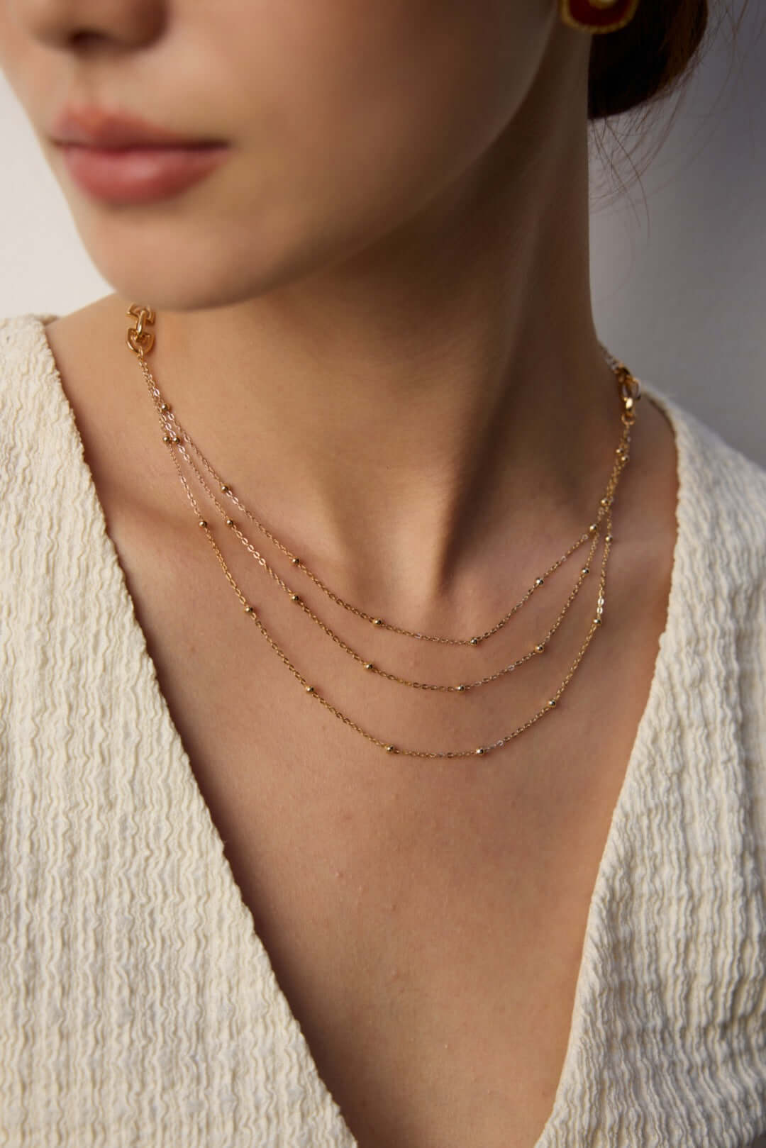 Mira Aura modern gold chain necklace triple layered delicate chains on model wearing cream top
