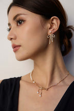 Model wearing Mira Aura modern pearl jewelry gold bow pendant necklace and matching pearl drop earrings
